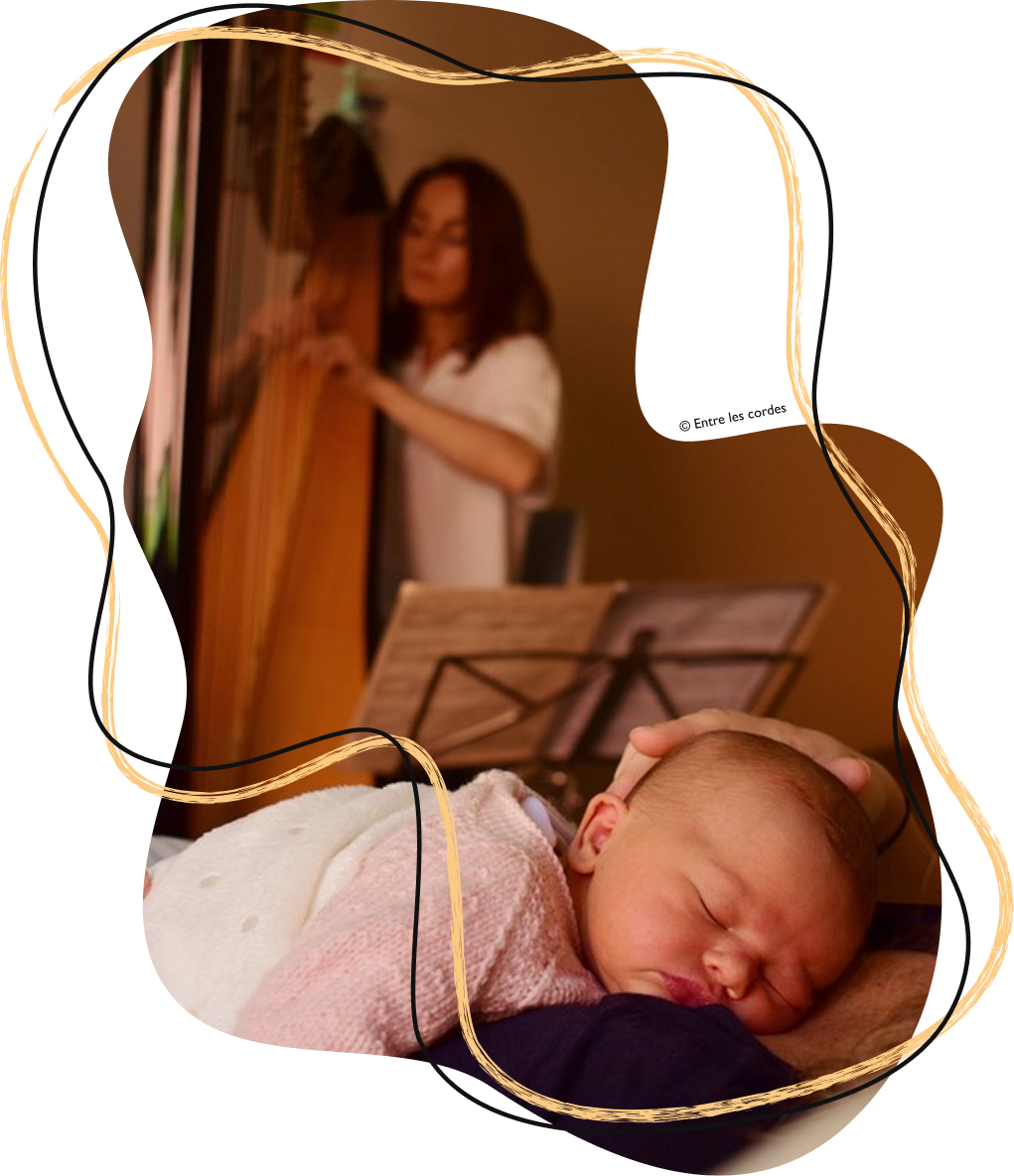Sophie Béguier jouant de la harpe dans le fond d'une chambre d'hôpital, avec un bébé endormi figurant au premier plan.